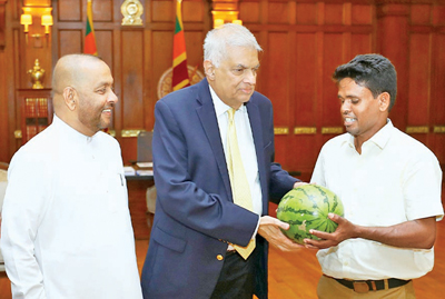 Farmer Budhika Sudarshana presents a watermelon from his harvest to President Ranil Wickremesinghe, as Agriculture and Plantation Industries Minister Mahinda Amaraweera looks on. 